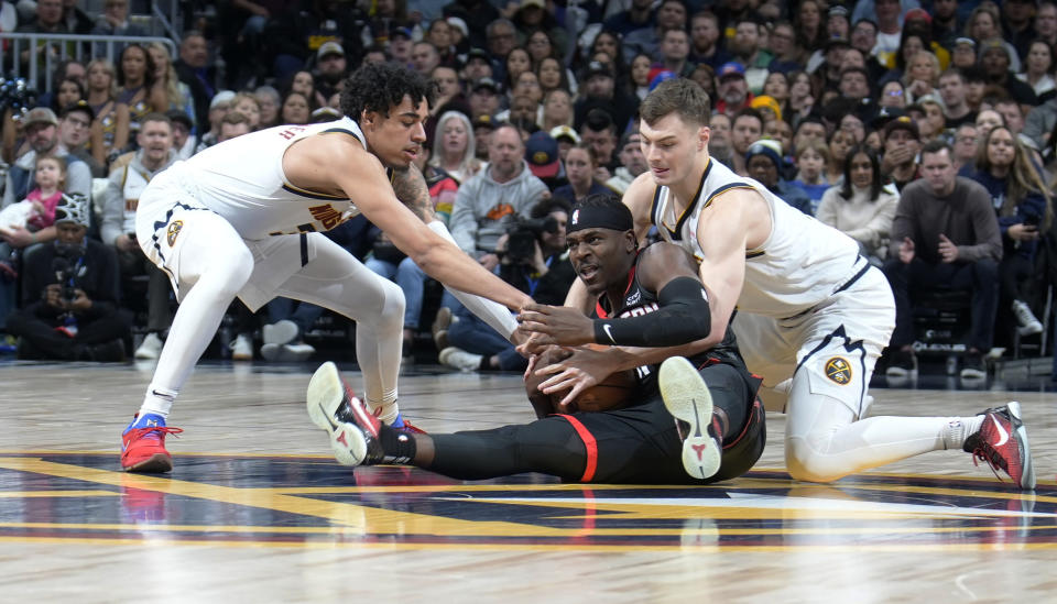 Houston Rockets guard Aaron Holiday, center, gathers in the ball as Denver Nuggets guards Julian Strawther, left, and Christian Braun defend during the first half of an NBA basketball game Friday, Dec. 8, 2023, in Denver. (AP Photo/David Zalubowski)