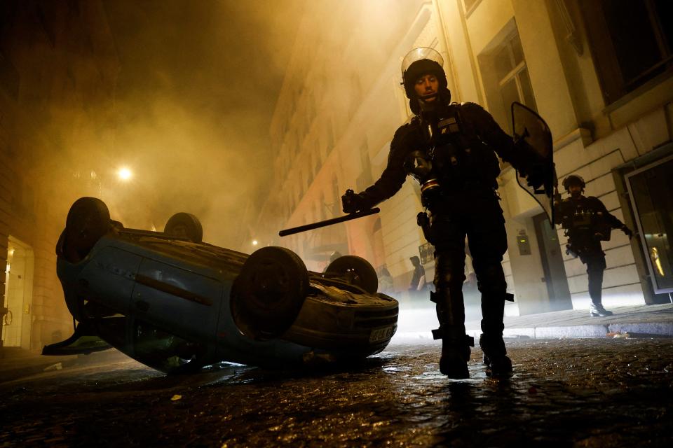 French riot police officers walk next to a vehicle upside down (REUTERS)