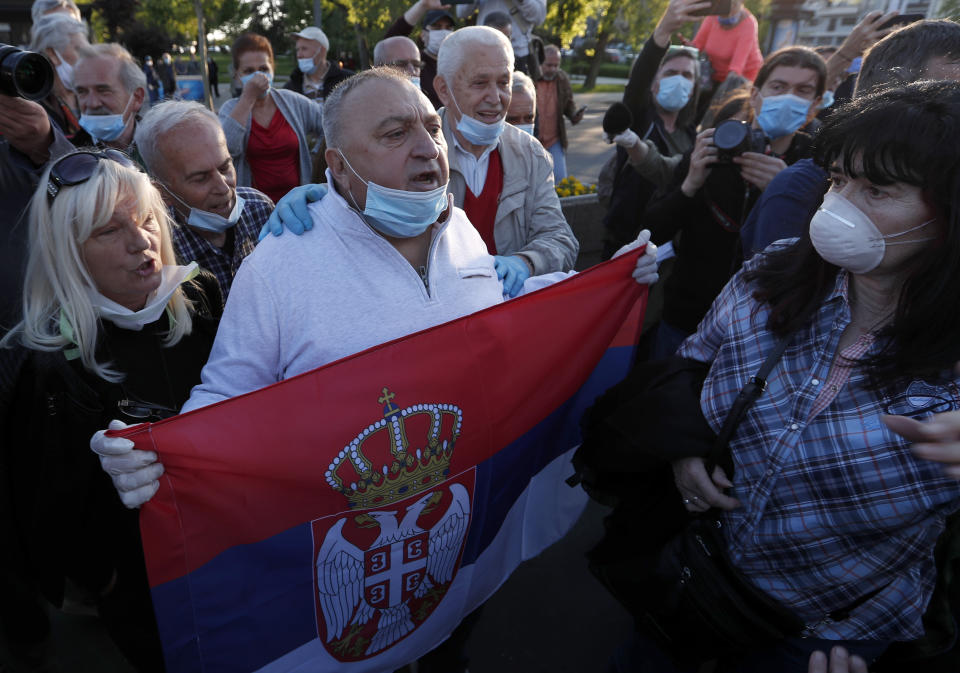 Government supporters hold a Serbian flag and shout slogans during a Serbian opposition leaders protest in front of the Serbian parliament building in Belgrade, Serbia, Thursday, April 30, 2020. Serbian opposition leaders gathered during an evening curfew to protest measures imposed by the populist authorities against the spread of the new coronavirus. Serbia's populist government in mid-March introduced some of the harshest measures in Europe, banning people over 65 years old from leaving their homes and imposing a daily and weekend curfews. (AP Photo/Darko Vojinovic)