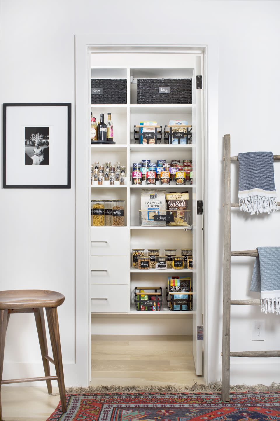 pantry organization ideas, tiered shelves in the white pantry with cans of food, labeled baskets, and glass jars