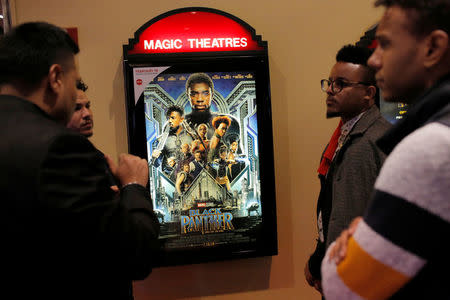 A group of men gather in front of a poster advertising the film "Black Panther" on its opening night of screenings at the AMC Magic Johnson Harlem 9 cinemas in Manhattan. REUTERS/Andrew Kelly