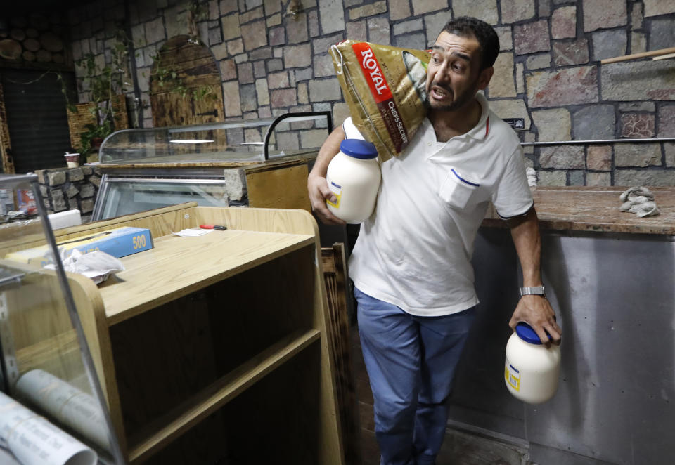 In this July 11, 2019, photo, Diaa Alhanoun, a refugee escaping war-torn Syria who has only been in the United States three years, carries a 40-pound bag of rice on his shoulders and bottles of mayonnaise while yelling instructions to his partner as the pair prepare for the opening of their restaurant Sakib, in New York. The restaurant, which features typical Mediterranean appetizers and dishes, is located along a main street in trendy Williamsburg, in the Brooklyn borough of New York. (AP Photo/Kathy Willens)