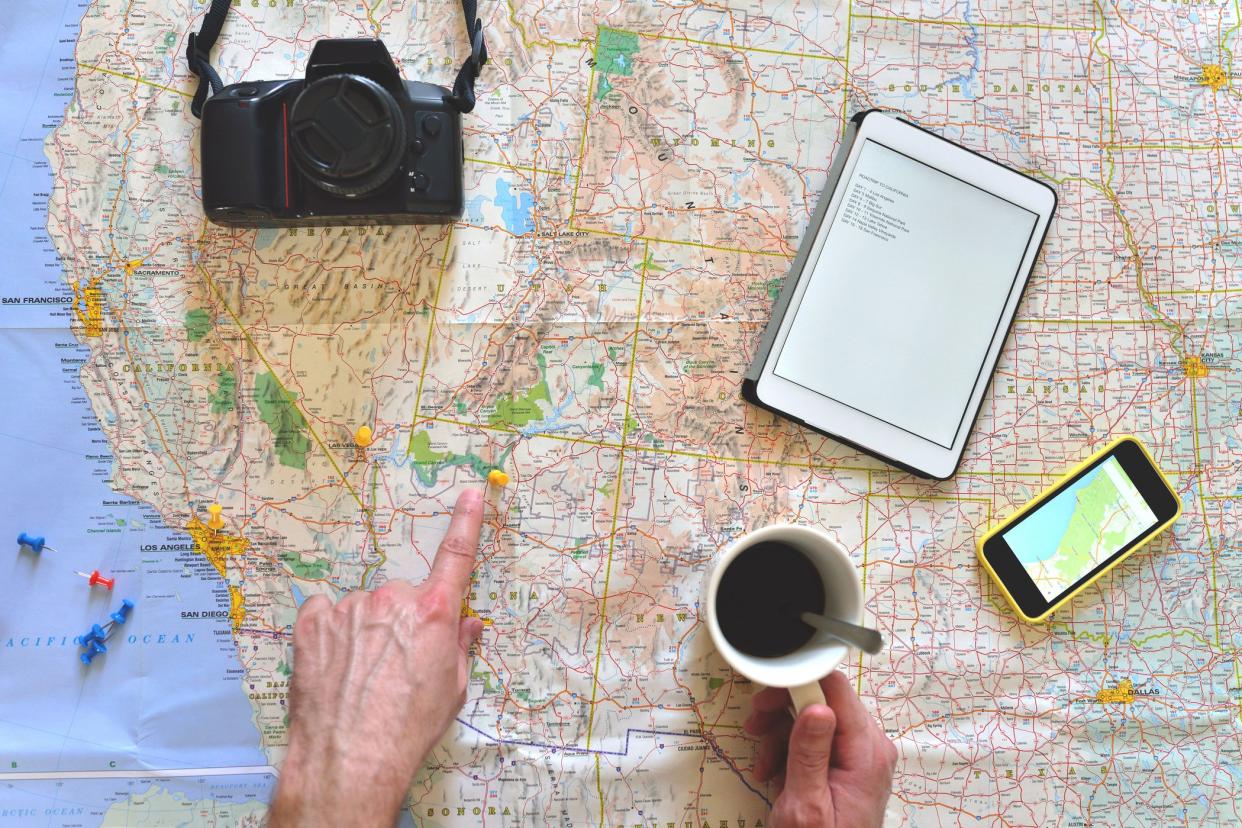 coffee cup, hands, pins, camera, phone, tablet over us map