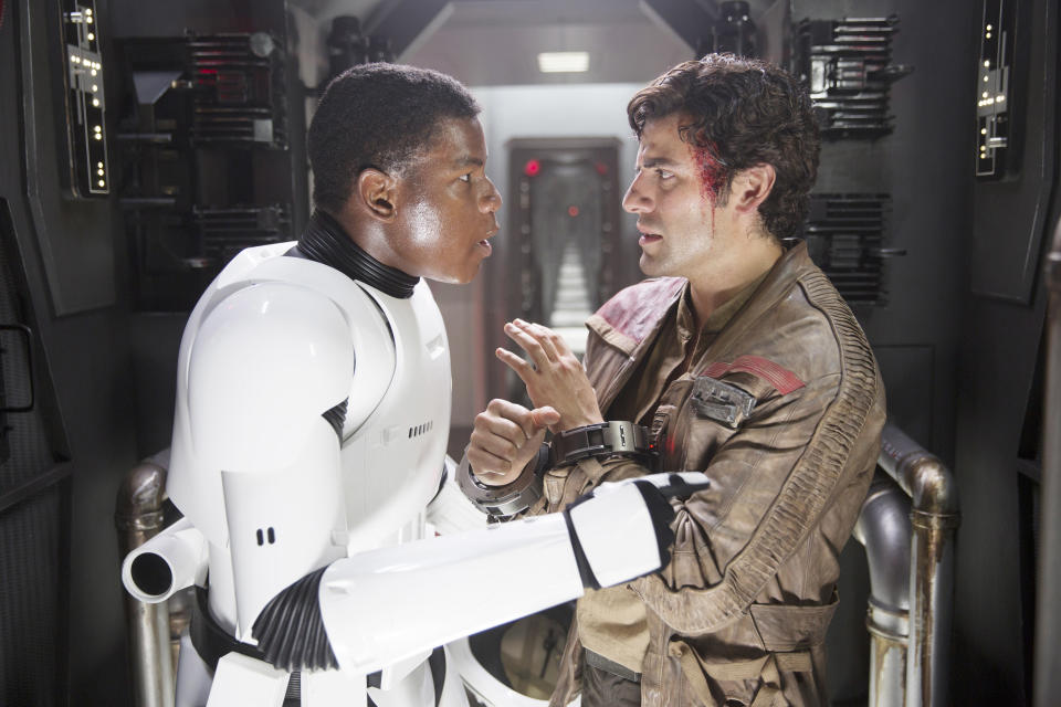 John Boyega, in a Stormtrooper suit, and Oscar Isaac, in a rugged outfit, stand face-to-face on a spaceship set from "Star Wars: The Force Awakens."