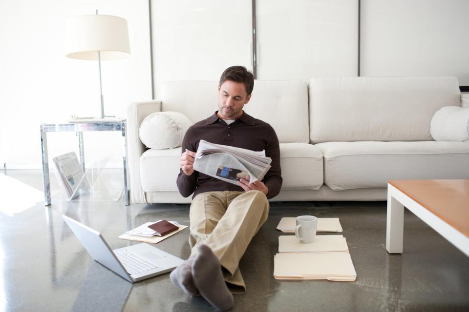 A person sitting by the couch reading the newspaper.