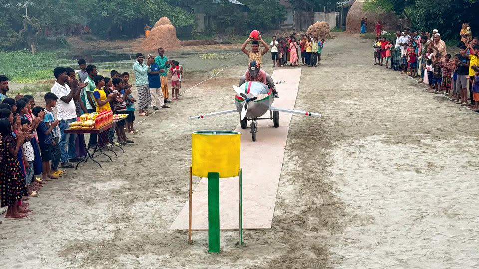 A player glides down a makeshift jet on cardboard runway, holding a ball and aiming for the basket during a game in Purandarpur village in the Pabna District of Bangladesh on October 17, 2023. - Courtesy Omar Sunny Somrat/SS Food Challenge