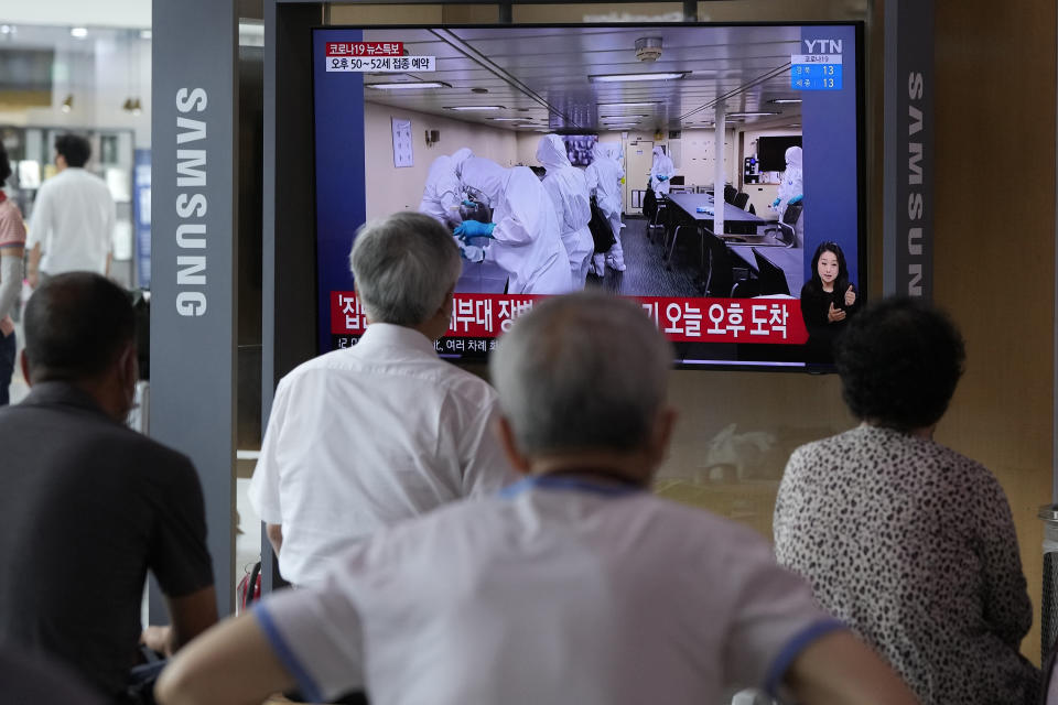 People watch a TV showing an image of South Korean service members wearing protective clothes disinfect inside the naval destroyer Munmu the Great during a news program at the Seoul Railway Station in Seoul, South Korea, Tuesday, July 20, 2021. South Korea's prime minister on Tuesday apologized for "failing to carefully take care of the health" of hundreds of sailors who contracted the coronavirus on a navy ship taking part in an anti-piracy mission off East Africa. (AP Photo/Ahn Young-joon)