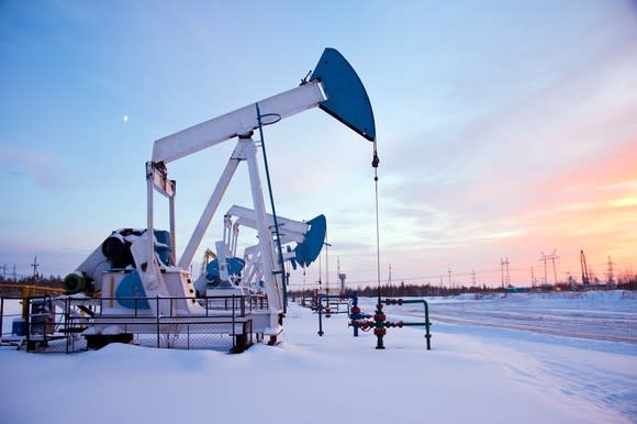 Giant pumpjack standing in snow at sunset.