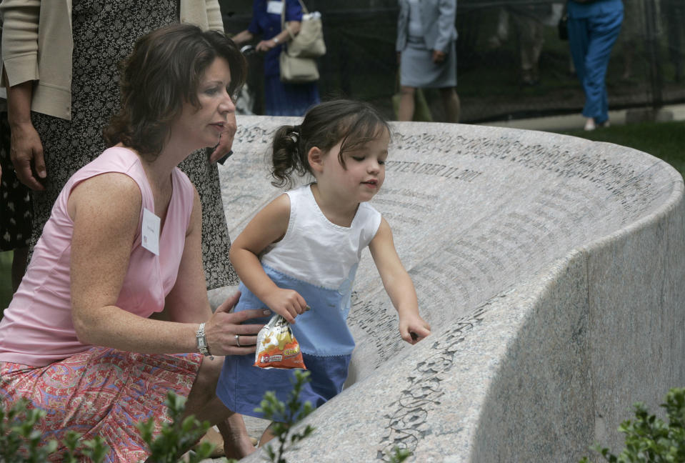 Leah Quigley, 2, touches the memorial in the Boston Public Garden in Boston, Monday, July 12, 2004, during a dedication ceremony of the memorial to the Massachusetts victims of the 9/11 terror attacks, as her mother Patti looks on. Patti Quigley's husband Patrick was killed in the Sept. 11, 2001, when Patti was a pregnant with Leah. (AP Photo/Chitose Suzuki)