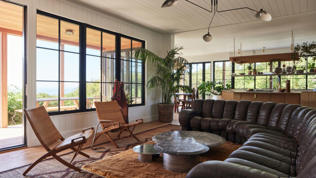  Living room with large black leather sofa, white walls, and earthy color palette furniture. 