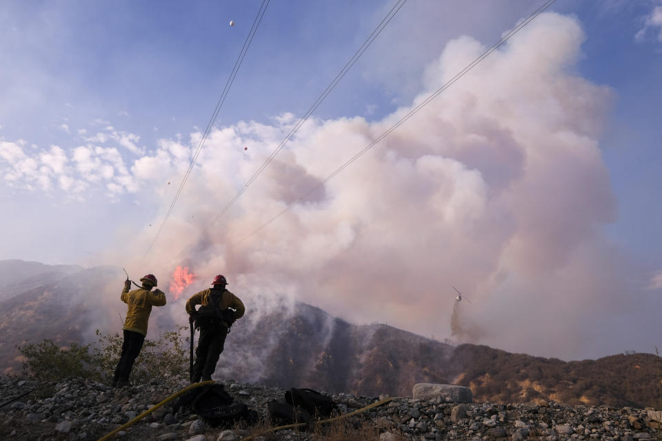 Firefighters watch as a helicopter drops water at the South Fire burning in Lytle Creek, San Bernardino County, north of Rialto, Calif., Wednesday, Aug. 25, 2021. (AP Photo/Ringo H.W. Chiu)