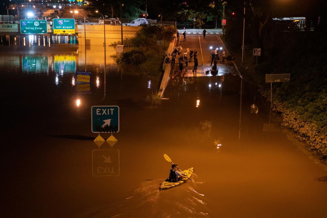 A kayaker paddles down a portion of a flooded highway.