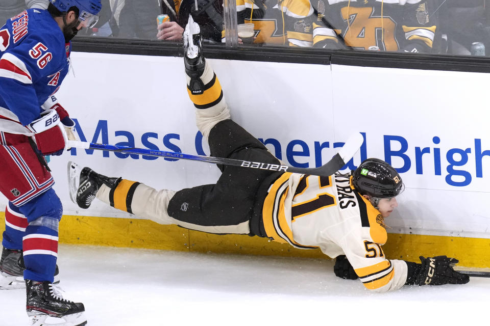 Boston Bruins center Matthew Poitras (51) is tripped up by New York Rangers defenseman Erik Gustafsson (56) during the second period of an NHL hockey game, Saturday, Dec. 16, 2023, in Boston. (AP Photo/Charles Krupa)