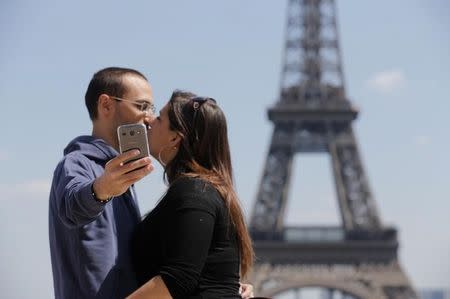 A couple of tourists use a mobile phone to take a selfie picture as they kiss at the Trocadero Square near the Eiffel Tower in Paris, May 16, 2014. REUTERS/Christian Hartmann