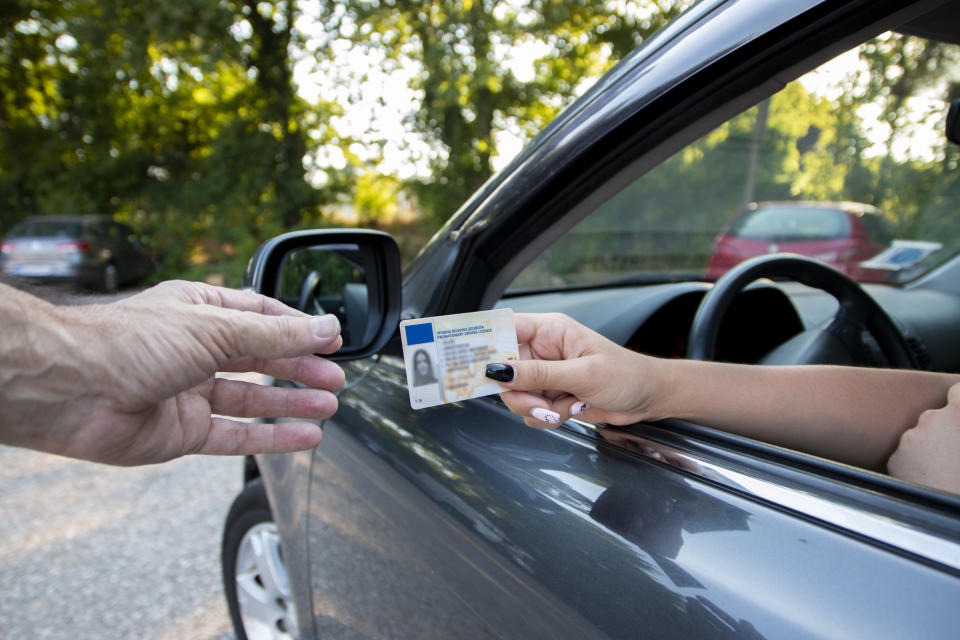 Two hands exchanging a driver's license at a car window