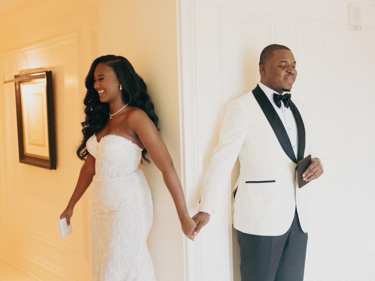 A bride and groom hold hands as they lean against two different walls for a first touch.