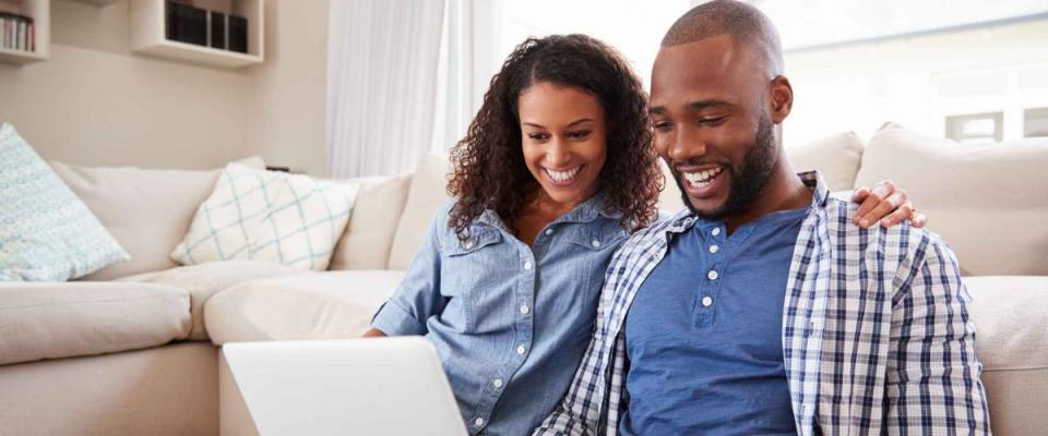 Young black couple using laptop sitting on the floor at home