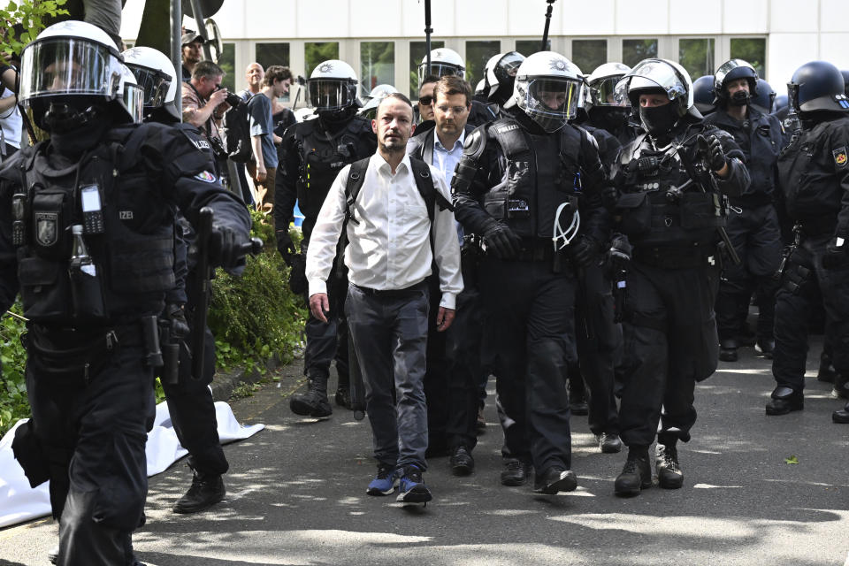 Participantes en el congreso federal del partido de ultraderecha AfD pasan, escoltados por la policía, junto a manifestantes, en Grugahalle, Essen, Alemania, el 29 de junio de 2024. (Henning Kaiser/dpa via AP)