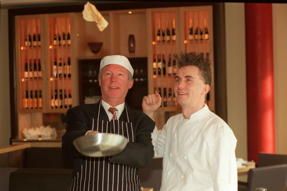 Manchester United manager Alex Ferguson (left) tosses a pancake at the opening of the Manchester United restaurant, cheered on by chef Gary Rhodes (right)  (Photo by Peter Wilcock/EMPICS via Getty Images)