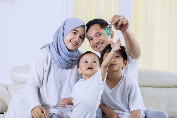 Muslim family looks happy while holding keys to their new home and sitting on the couch