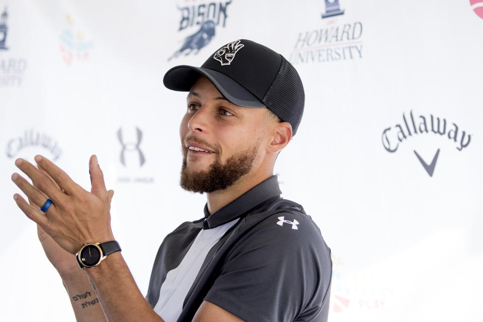 The Under Armor, Callaway, and Howard University Bison logos are visible behind Golden State Warriors guard Stephen Curry as he applauds during a news conference at Langston Golf Course in Washington, Monday, Aug. 19, 2019, where Curry announced that he would be sponsoring the creation of men's and women's golf teams at Howard University. (AP Photo/Andrew Harnik)