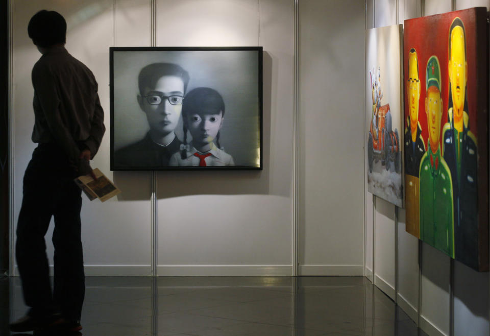 A man walks past a painting titled "Bloodline Series", center, by Chinese artist Zhang Xiaogang at the Seoul Auction in Hong Kong Tuesday, April 3, 2012. Auctioneers in Hong Kong have sold 10 paintings seized from a South Korean bank that collapsed last year amid a corruption scandal to raise $2.4 million to help repay depositors. The paintings included works by noted Chinese artists Zeng Fanzhi and Zhang Xiaogang and American Julian Schnabel. (AP Photo/Kin Cheung)