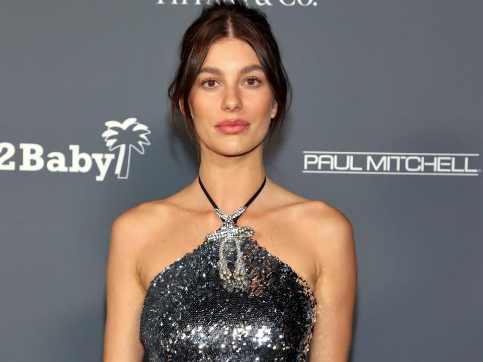 Camila Morrone poses on the red carpet in a gray sparkly halter dress.