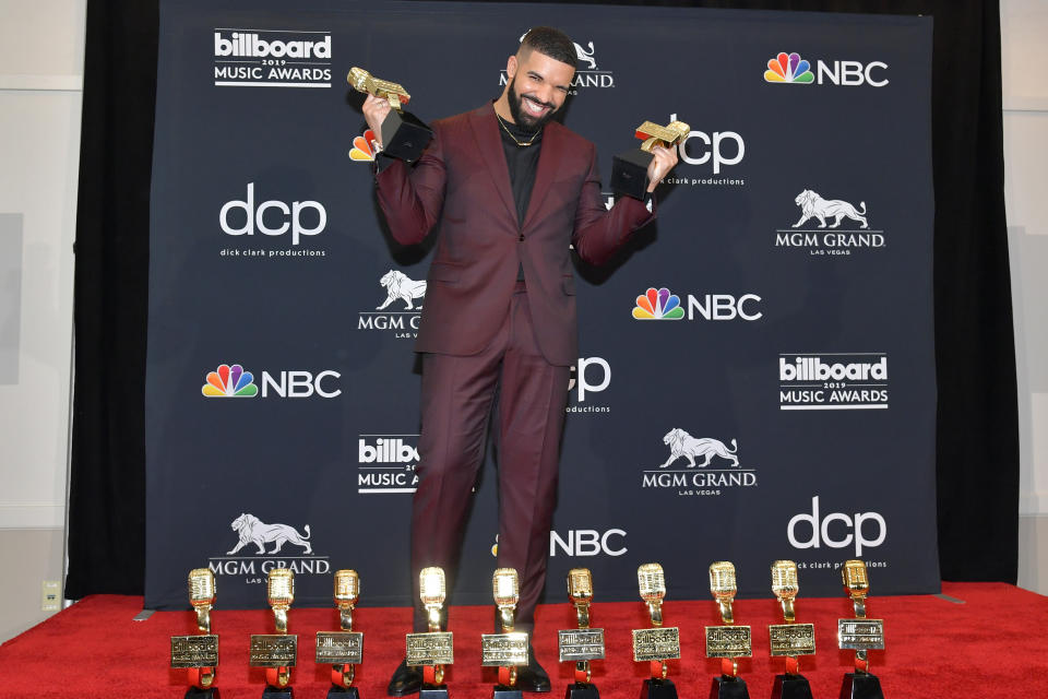 Drake wearing maroon suit posing with awards.