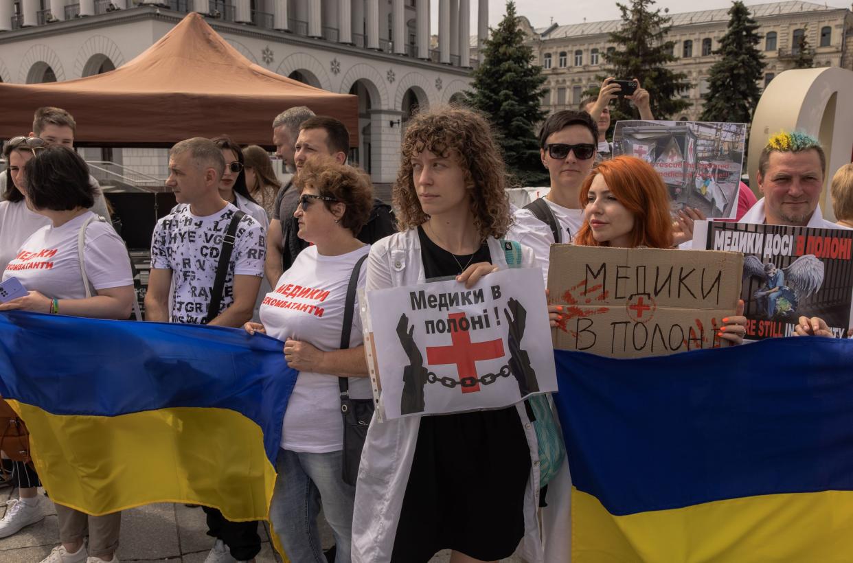 Relatives, friends and members of the public hold Ukrainian flags and placards reading 