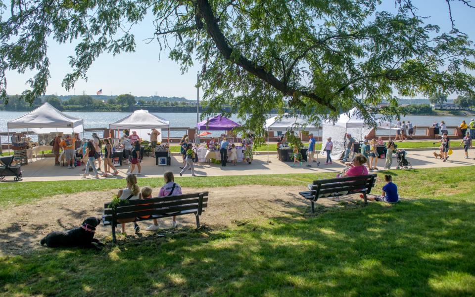 Patrons relax in the shade of a large tree while taking a break from shopping at the weekly Riverfront Market in Peoria.