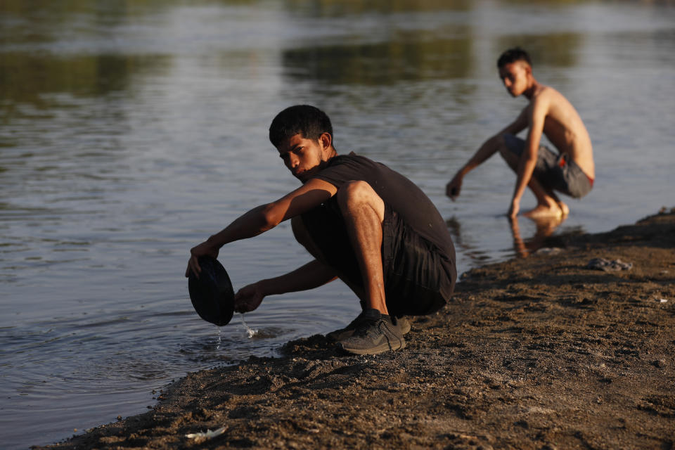 A Honduran migrant washes a plate as he prepares to fry eggs, at the Suchiate River which creates a natural border between Guatemala and Mexico, near Tecun Uman, Guatemala, Wednesday, Jan. 22, 2020. The number of migrants stuck at the Guatemala-Mexico border continued to dwindle Wednesday as detentions and resignation ate away at what remained of the latest caravan. (AP Photo/Marco Ugarte)