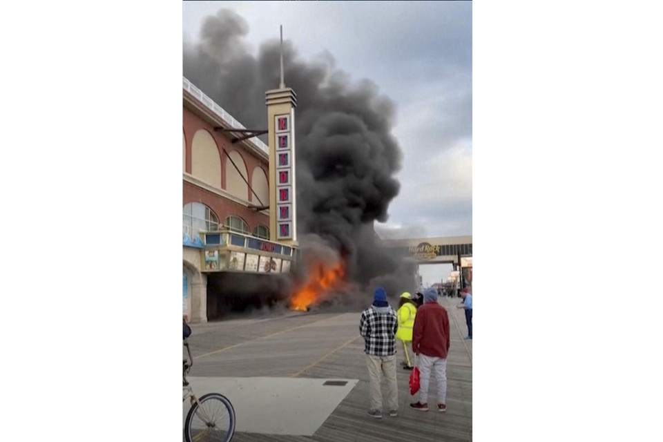 In this image taken from video provided by Aris Matos, flames rise from under the wooden Atlantic City Boardwalk, Wednesday, Nov. 15, 2023, in front of the entrance to Resorts casino. Investigators were trying Thursday to determine what touched off the fire on the boardwalk that burned a section of the historic walkway and damaged part of the casino's facade. (Aris Matos via AP)