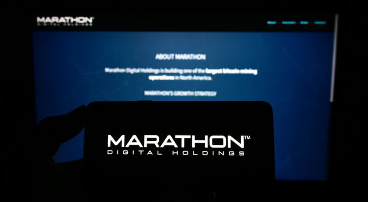 Person holding mobile phone with logo of American company Marathon Digital Holdings Inc. on screen in front of web page. Focus on phone display. Unmodified photo. MARA stock