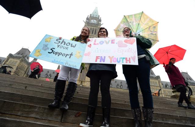Three women stand together holding signs that read &#39;show your support&#39; and &#39;love first nations youth&#39;