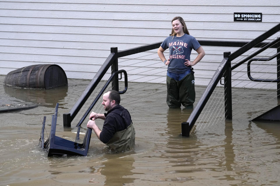 FILE - Nathan Sennett and Tori Grasse retrieve furniture from a flooded patio near the Kennebec River, Tuesday, Dec. 19, 2023, in Hallowell, Maine. Unseasonably warm weather, including rain storms in the northeast, is washing away snow at ski areas and reducing the chances that many people in the U.S. will experience a white Christmas this year. (AP Photo/Robert F. Bukaty, File)