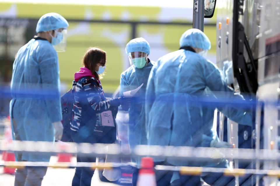 Staffs in protective suits escort a passenger disembarked from the quarantined Diamond Princess cruise ship at a port in Yokohama, near Tokyo, Friday, Feb. 21, 2020. Passengers tested negative for COVID-19 started disembarking since Wednesday. (AP Photo/Eugene Hoshiko)