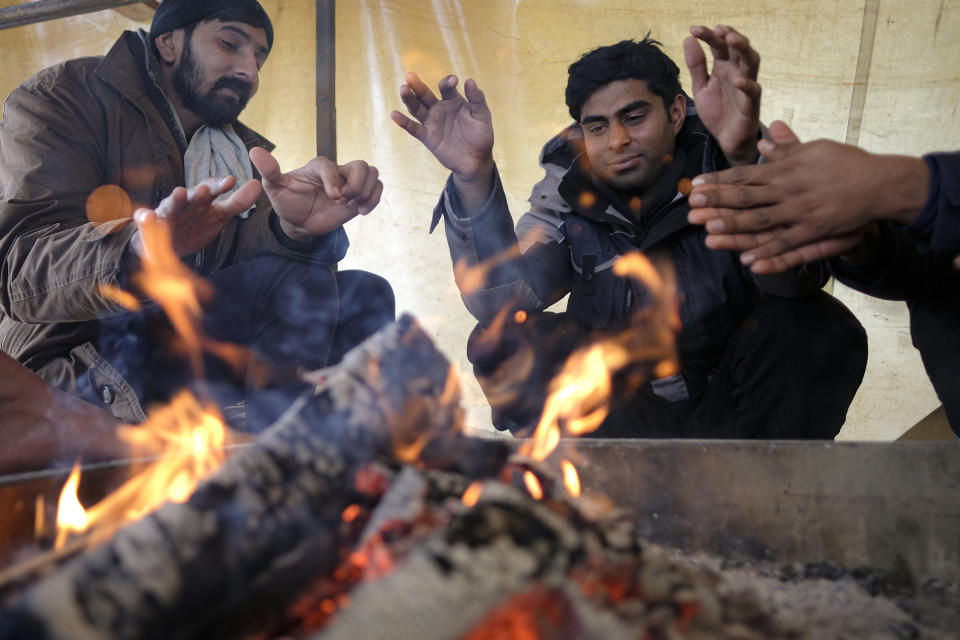 Migrants warm themselves around a fire in a makeshift tent at the Lipa camp, outside Bihac, Bosnia, Friday, Jan. 8, 2021. A fresh spate of snowy and very cold winter weather on has brought more misery for hundreds of migrants who have been stuck for days in a burnt out camp in northwest Bosnia waiting for heating and other facilities. (AP Photo/Kemal Softic)