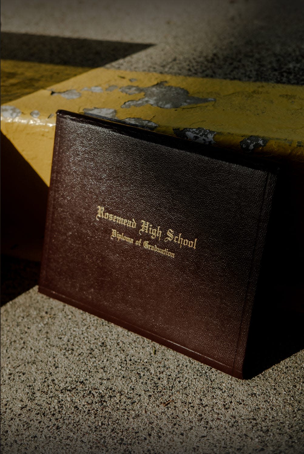 A leather Rosemead High diploma case rests against cement school steps.