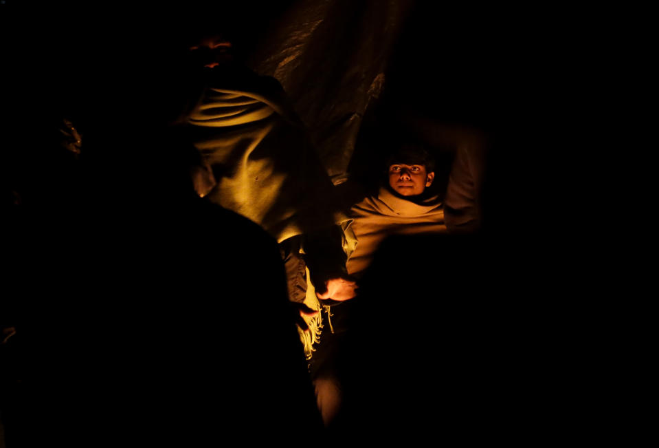 In this Sunday, Nov. 18, 2019 photo a migrant boy tries to stay warm sitting next to a fire at a camp in Velika Kladusa, Bosnia, close to the border to Croatia. The approach of the tough Balkan winter spells tough times for the migrants that remain stuck in the region while trying to reach Western Europe, with hundreds of them staying in make-shift camps with no heating or facilities.(AP Photo/Amel Emric)