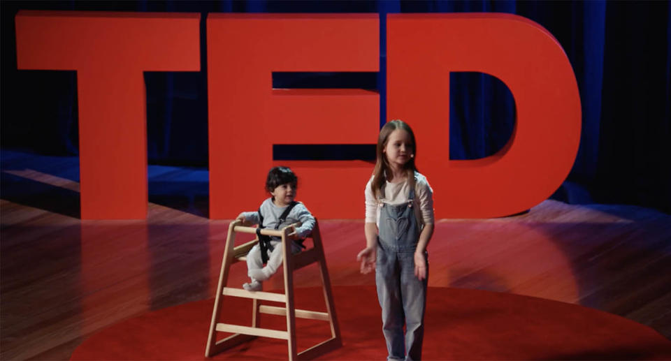 A screenshot from Molly Wright's TED talk showing her in front of th TED sign with her neighbour, baby Ari who she talked about in her talk.