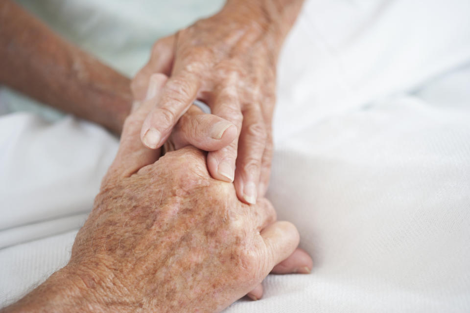 A close-up of a younger person's hand holding an elderly person's hand, offering comfort or support