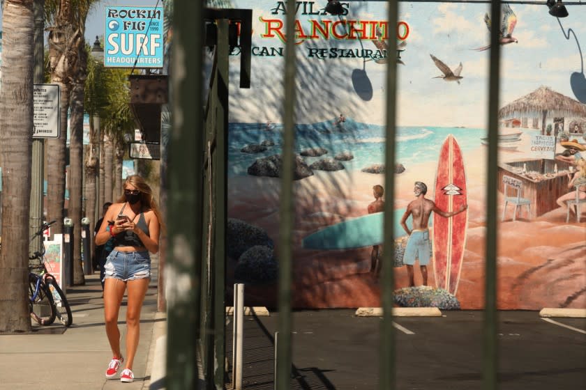 HUNTINGTON BEACH, CA - AUGUST 12, 2020 - - A masked pedestrian walks along Main Street during a "Masks Up, Surf City," banner campaign to prevent coronavirus in Huntington Beach on August 12, 2020. The campaign, a play on the phrase "Surf's Up," includes 100 pennants, a banner at the pier and digital displays citywide, Huntington Beach spokeswoman Catherine Jun said. Fifty pennants were installed downtown on Aug. 6. The remaining signs are in production this week, and 13 pennants and a banner are expected to be installed on the Huntington Beach Pier. (Genaro Molina / Los Angeles Times)