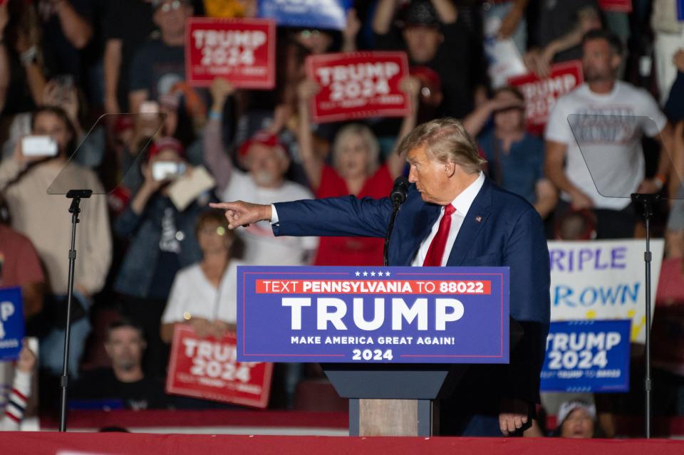 Former President Trump points a finger while standing at a podium at a campaign rally.