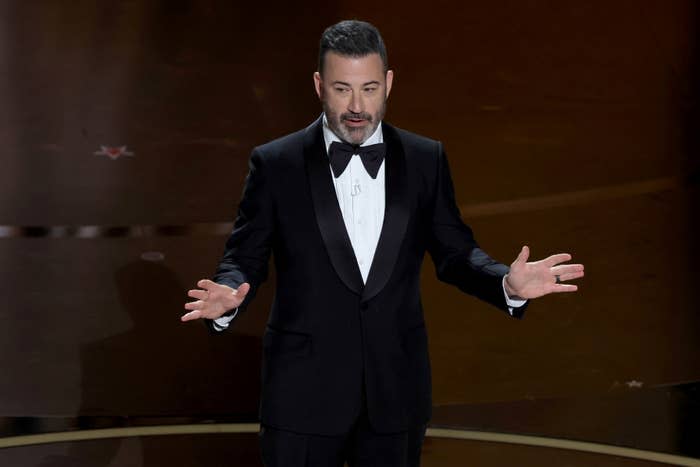 Man in a tuxedo on stage speaking, possibly hosting an event