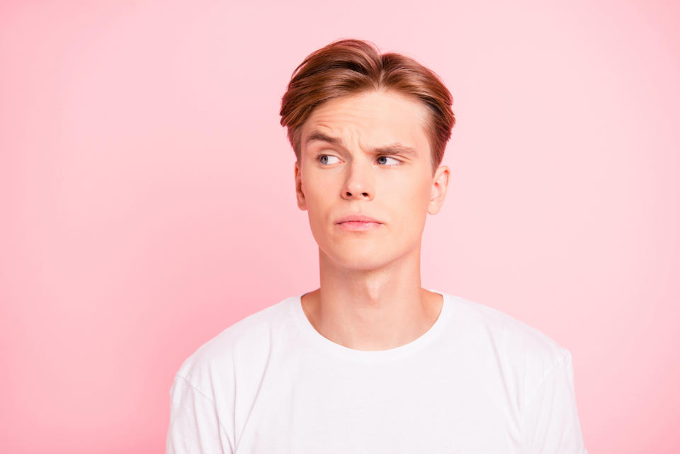 Man in white t-shirt against pink background raising an eyebrow