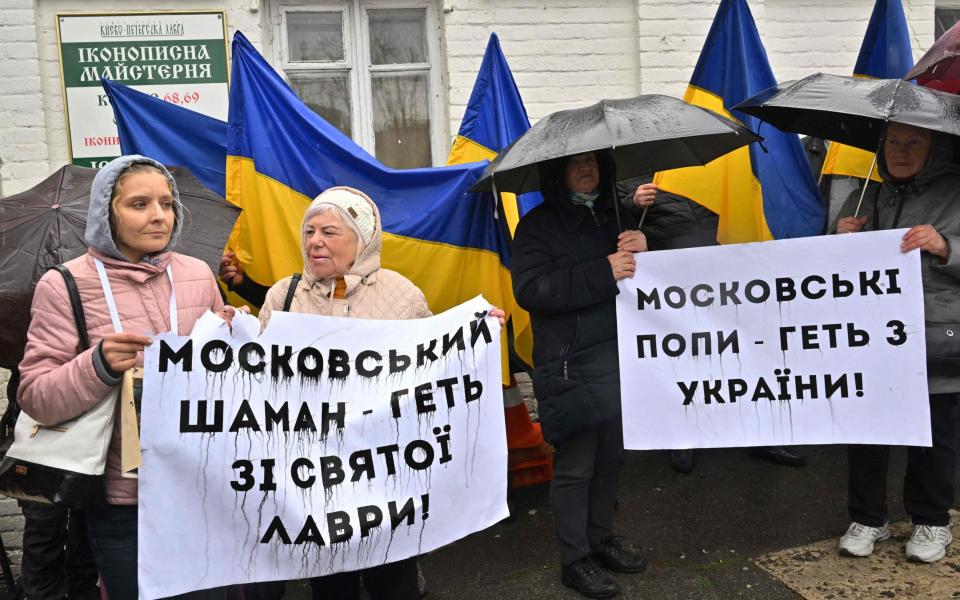 People hold placards reading "Moscow priests get away from Ukraine!" (R) and "Moscow shaman get away from holy Lavra!" as they rally at the entrance to the Kyiv-Pechersk Lavra - SERGEI SUPINSKY/AFP