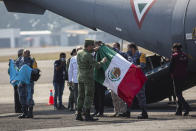 Miembros de las Fuerzas Armadas Mexicanas despliegan una bandera nacional mexicana junto al avión que transportaba los restos de migrantes guatemaltecos muertos en un accidente de camión en el sur de México, en la pista del Aeropuerto Internacional La Aurora en la Ciudad de Guatemala, el jueves 30 de diciembre de 2021. (AP Foto/Oliver de Ros)