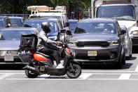 A delivery driver on a scooter rides the pedestrian crosswalk through traffic on a delivery in the Seaport District, Friday, June 7, 2024, in Boston. A soaring demand for food delivered fast has spawned small armies of couriers in a growing number of cities where delivery scooters, motorcycles and mopeds zip in and out of traffic and hop onto sidewalks alongside startled pedestrians racing to drop off salads and sandwiches. (AP Photo/Charles Krupa)