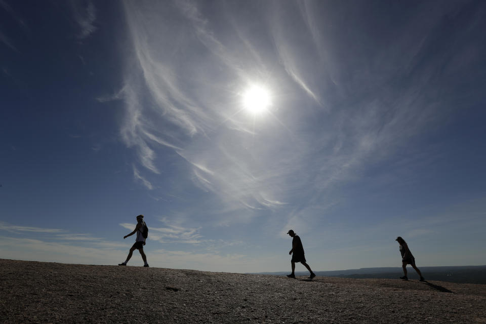 Following social distancing rules and wearing face coverings, visitors hike through Enchanted Rock State Park, Monday, April 20, 2020, in Fredericksburg, Texas. Texas state parks are reopened to the public Monday after they had been closed due to the COVID-19 pandemic, but visitors must follow social distancing rules and wear a facial covering or mask. (AP Photo/Eric Gay)