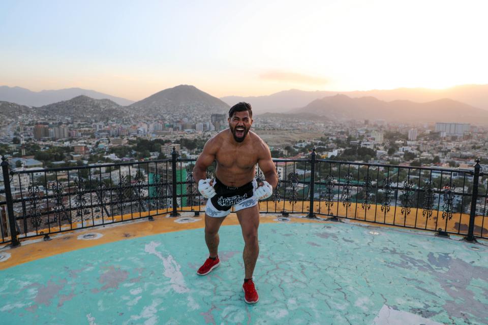 A shirtless man flexes his muscles with the Kabul skyline visible in the background.